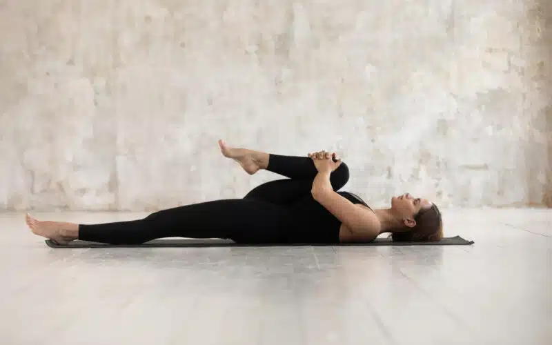 Woman pulls in each leg to stretch back