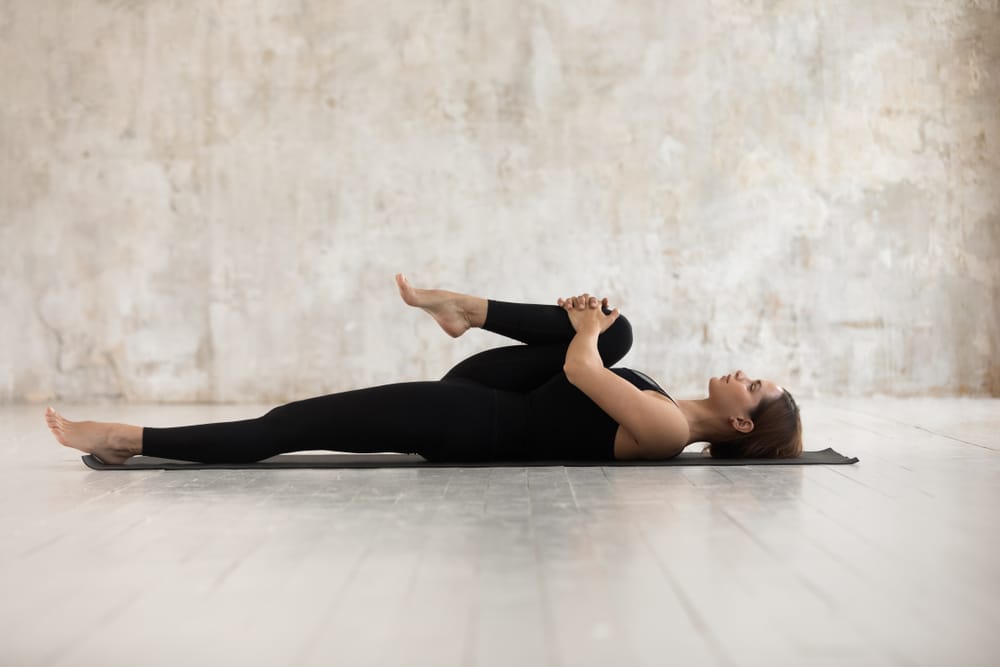 Woman pulls in each leg to stretch back